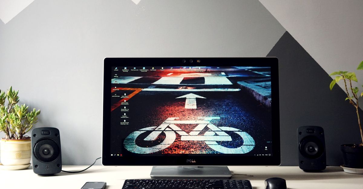 Sleek desktop setup featuring a monitor with urban cycling wallpaper, surrounded by speakers and plants.